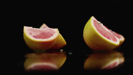 One-juicy-sliced-​​grapefruit-falling-on-a-glass-with-water-splashes-in-slow-motion-on-a-dark-background